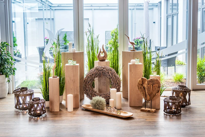 Fünfköpfige Familie mit drei Kindern, zwei Erwachsene, bei einem jungen Baum im Garten. Blumen, Pflanzen und Haus im Hintergrund sichtbar.